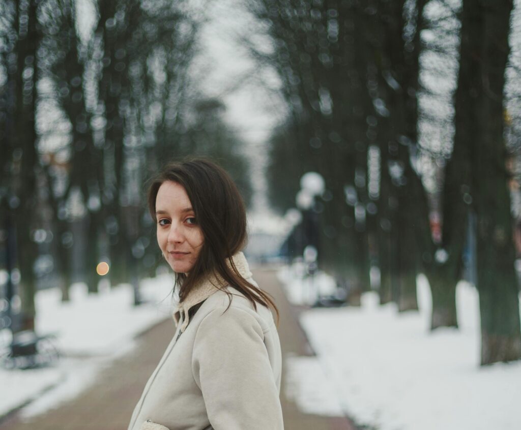 Woman wearing a cream-colored winter coat standing in a snowy park, showcasing stylish parka for extreme cold